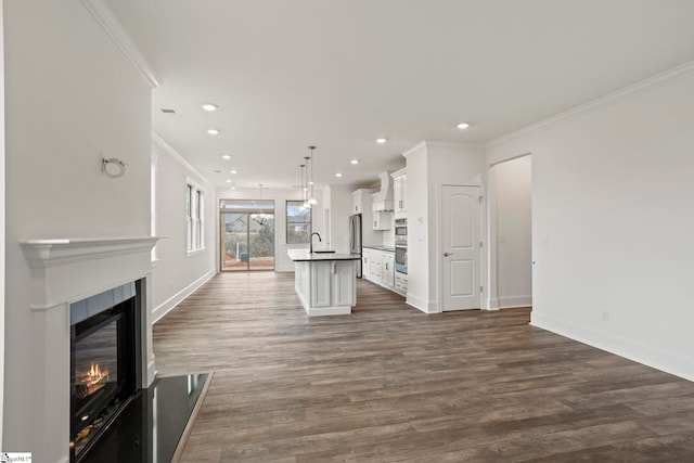 kitchen with white cabinetry, an island with sink, a glass covered fireplace, decorative light fixtures, and crown molding