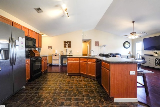 kitchen featuring an island with sink, lofted ceiling, a breakfast bar area, ceiling fan, and black appliances