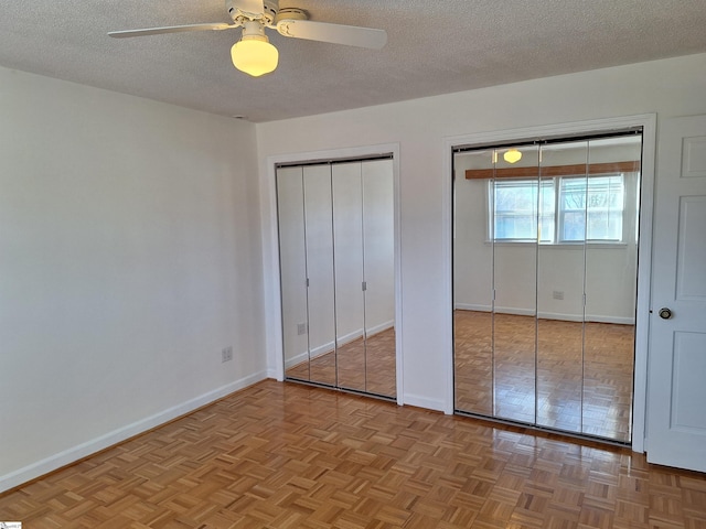 unfurnished bedroom featuring a ceiling fan, baseboards, multiple closets, and a textured ceiling