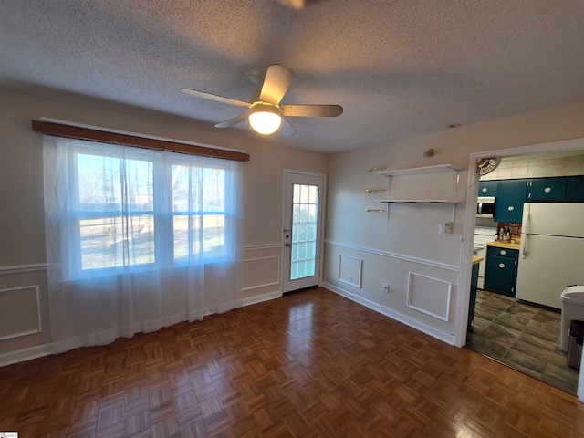 interior space featuring a textured ceiling, wainscoting, and ceiling fan