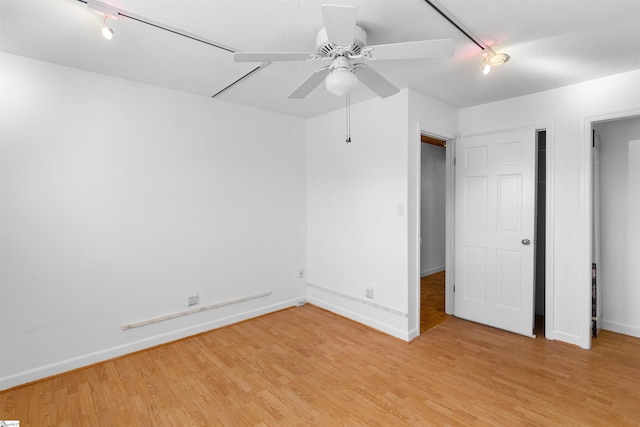 unfurnished bedroom featuring ceiling fan, rail lighting, light wood-type flooring, and baseboards