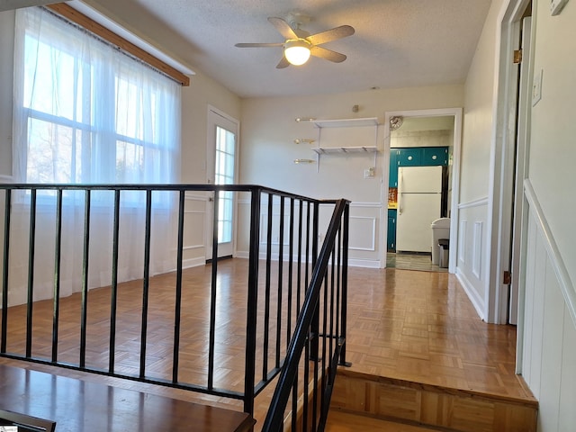 hall featuring an upstairs landing, a decorative wall, wainscoting, and a textured ceiling