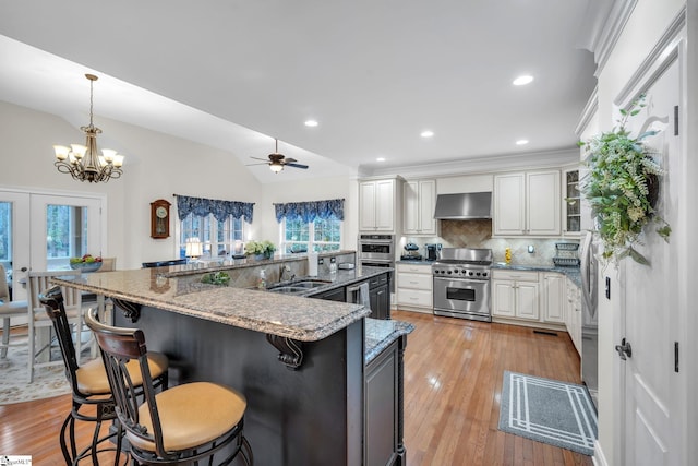 kitchen featuring a kitchen bar, decorative light fixtures, ventilation hood, stainless steel appliances, and white cabinets