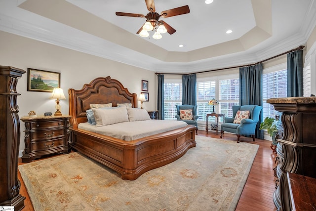 bedroom featuring hardwood / wood-style flooring, ceiling fan, ornamental molding, and a tray ceiling