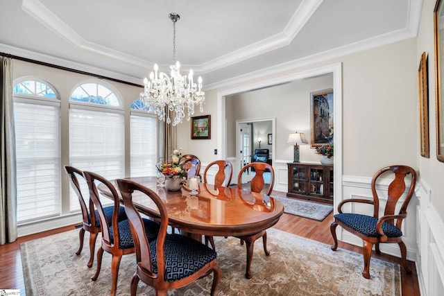 dining space with crown molding, hardwood / wood-style floors, a tray ceiling, and a chandelier