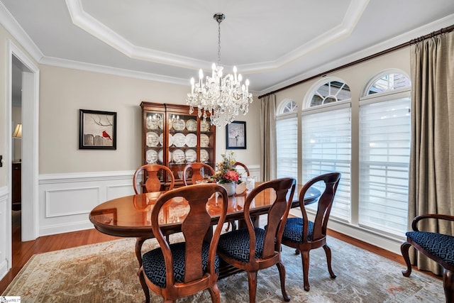 dining space featuring crown molding, a tray ceiling, an inviting chandelier, and light wood-type flooring