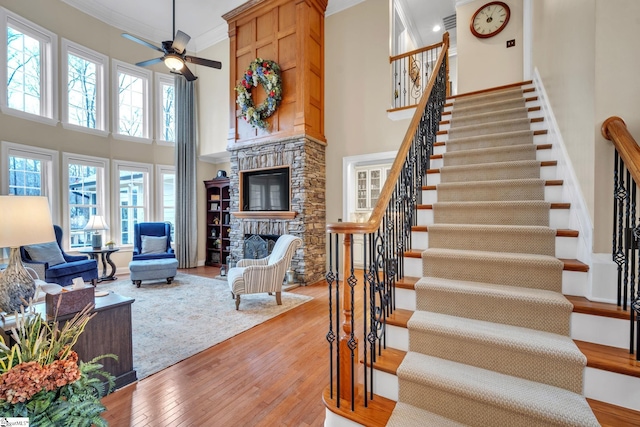 stairs featuring hardwood / wood-style flooring, a towering ceiling, ornamental molding, and a fireplace