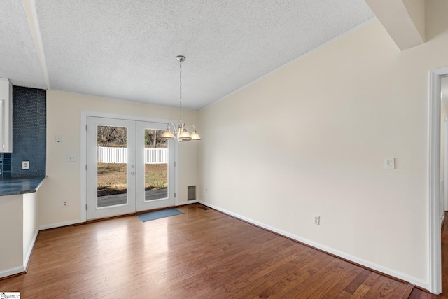 unfurnished dining area featuring wood-type flooring, a textured ceiling, a chandelier, and french doors