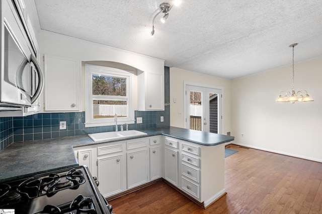 kitchen featuring range with gas stovetop, decorative light fixtures, sink, white cabinets, and kitchen peninsula