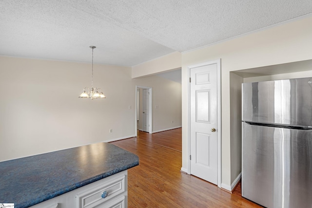 kitchen with an inviting chandelier, decorative light fixtures, stainless steel fridge, hardwood / wood-style flooring, and white cabinets