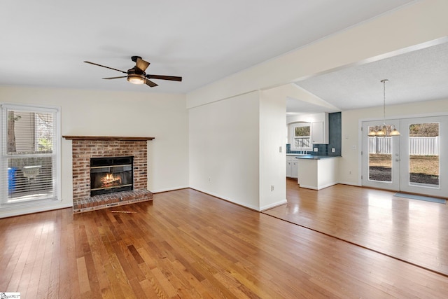 unfurnished living room featuring hardwood / wood-style flooring, ceiling fan with notable chandelier, and a fireplace