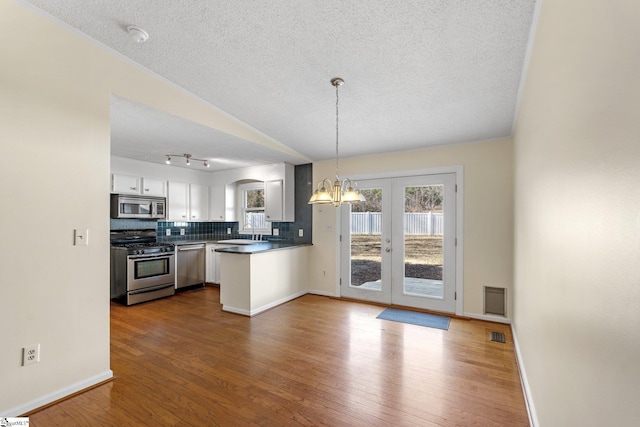 kitchen featuring appliances with stainless steel finishes, decorative light fixtures, sink, white cabinets, and backsplash