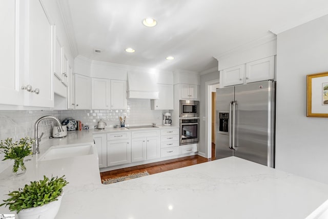 kitchen featuring premium range hood, sink, stainless steel appliances, decorative backsplash, and white cabinets