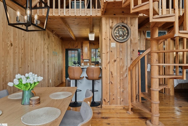 dining room featuring hardwood / wood-style flooring, a notable chandelier, beam ceiling, and wood walls