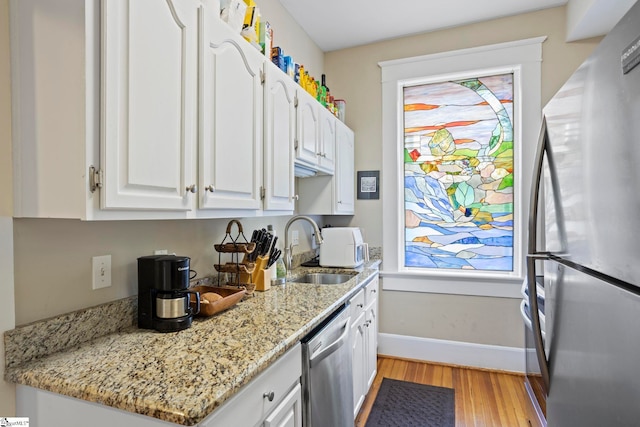 kitchen with stainless steel appliances, white cabinetry, light stone countertops, and sink