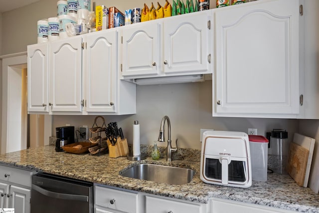 kitchen featuring light stone counters, dishwasher, sink, and white cabinets