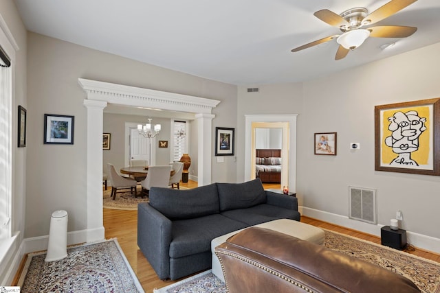 living room featuring ornate columns, ceiling fan with notable chandelier, and light hardwood / wood-style floors