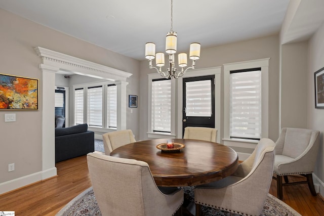 dining area with decorative columns, a notable chandelier, and light hardwood / wood-style floors