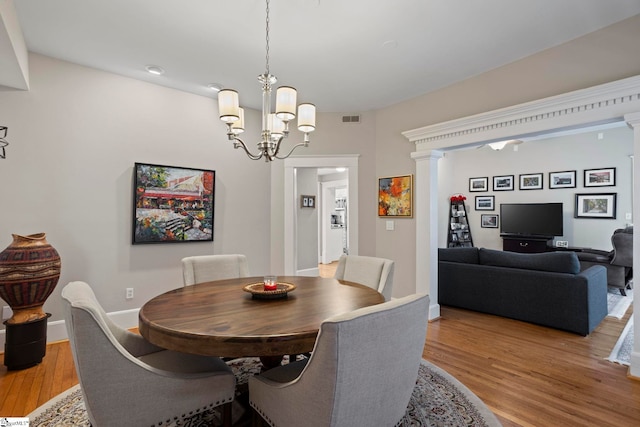 dining area with decorative columns, a notable chandelier, and light wood-type flooring