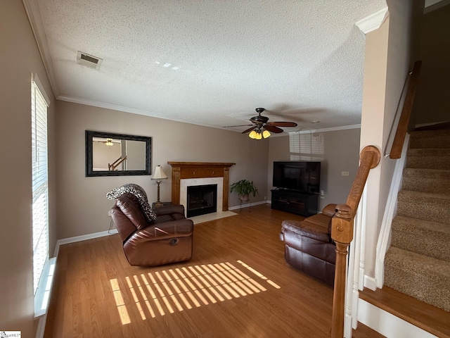 living room featuring hardwood / wood-style flooring, a fireplace, ornamental molding, and a textured ceiling