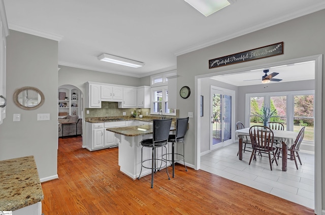 kitchen featuring a breakfast bar area, white cabinets, ornamental molding, kitchen peninsula, and light wood-type flooring