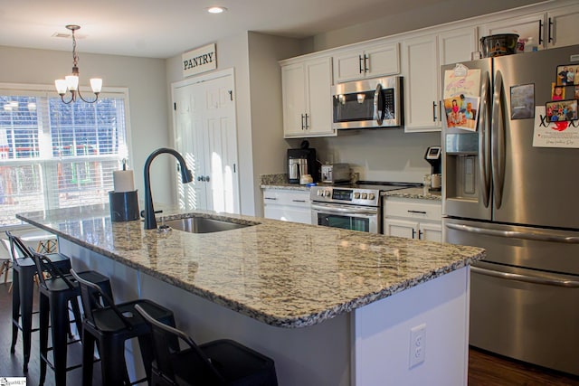 kitchen with sink, a center island with sink, hanging light fixtures, appliances with stainless steel finishes, and white cabinets