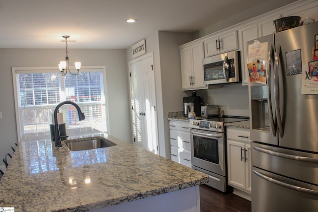 kitchen with appliances with stainless steel finishes, pendant lighting, white cabinetry, sink, and a center island with sink