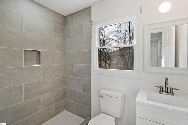 bathroom featuring vanity, a tile shower, and toilet