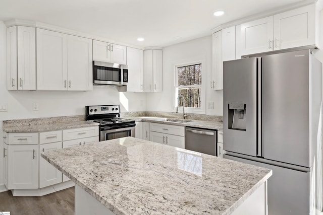 kitchen with appliances with stainless steel finishes, sink, white cabinets, light stone counters, and light hardwood / wood-style floors