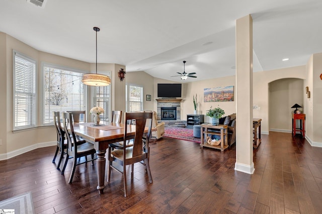 dining area with a fireplace, dark wood-type flooring, vaulted ceiling, and a healthy amount of sunlight