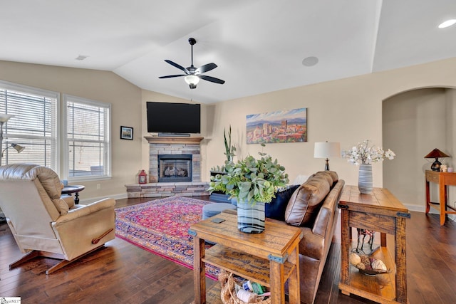 living room featuring dark hardwood / wood-style flooring, ceiling fan, a stone fireplace, and lofted ceiling