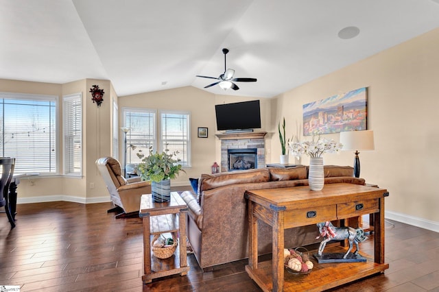 living room featuring ceiling fan, vaulted ceiling, dark hardwood / wood-style flooring, and a stone fireplace