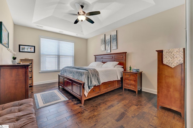 bedroom with a tray ceiling, ceiling fan, and dark wood-type flooring