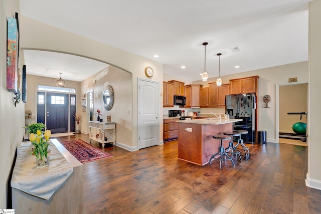 kitchen with a kitchen island with sink, decorative light fixtures, black appliances, a kitchen bar, and dark hardwood / wood-style floors