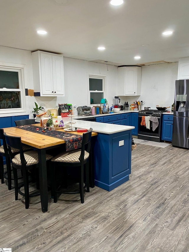 kitchen with stainless steel refrigerator with ice dispenser, blue cabinets, white cabinetry, light hardwood / wood-style flooring, and range with gas stovetop