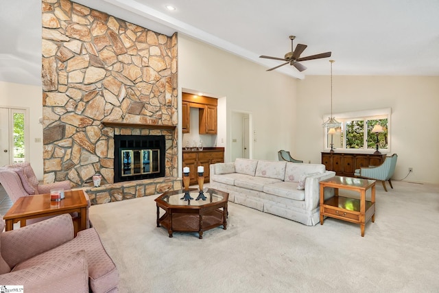 carpeted living room featuring a healthy amount of sunlight, ceiling fan, high vaulted ceiling, and a stone fireplace