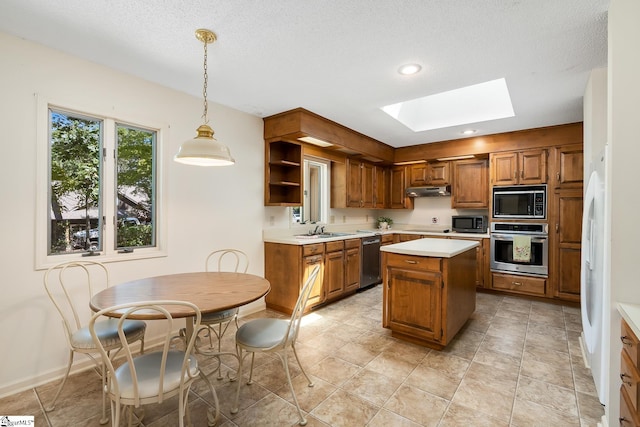 kitchen featuring stainless steel appliances, a skylight, decorative light fixtures, a kitchen island, and sink