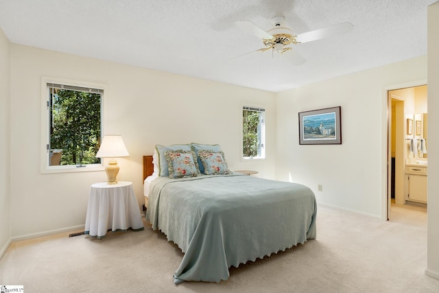 bedroom featuring ceiling fan, a textured ceiling, ensuite bath, and light colored carpet