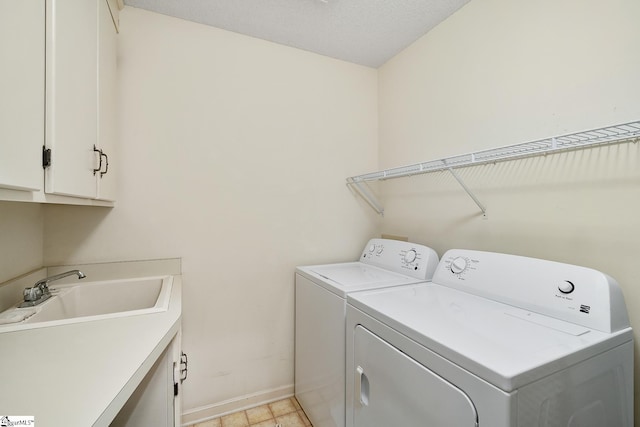 laundry room with washing machine and clothes dryer, sink, cabinets, and a textured ceiling