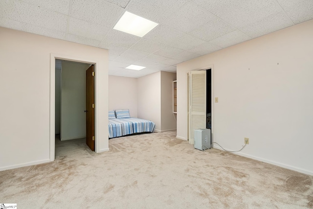 unfurnished bedroom featuring light carpet, a closet, and a drop ceiling