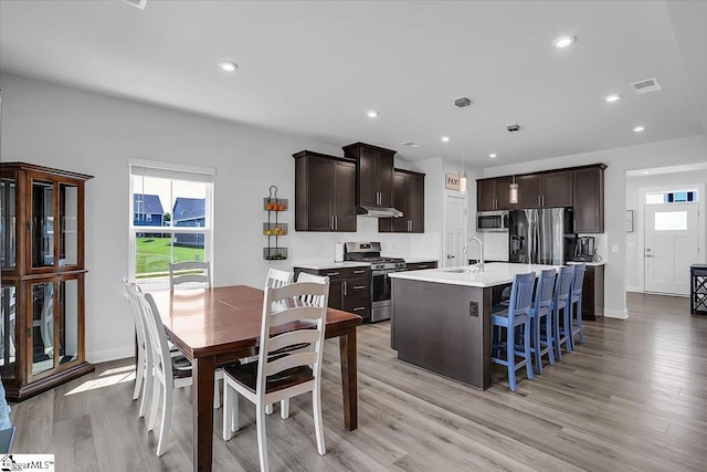 kitchen with appliances with stainless steel finishes, decorative light fixtures, an island with sink, and dark brown cabinets