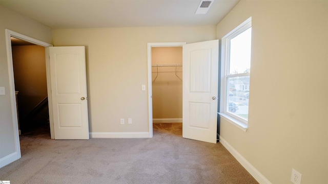 unfurnished bedroom with a closet, light colored carpet, and a spacious closet