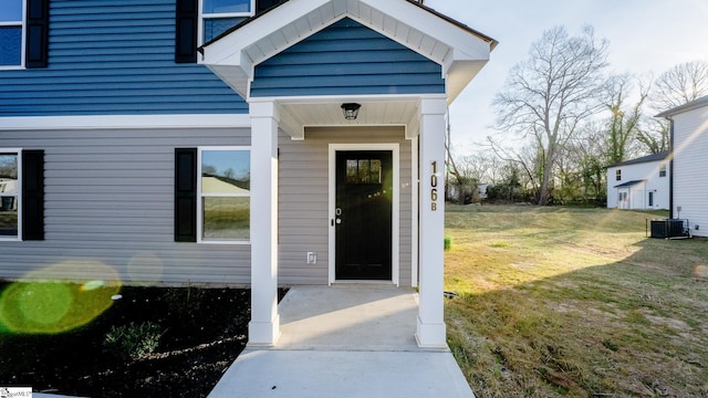 view of exterior entry with central AC and a lawn