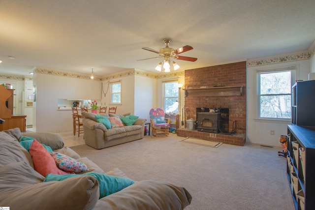 carpeted living room featuring a wood stove, ceiling fan, and a textured ceiling