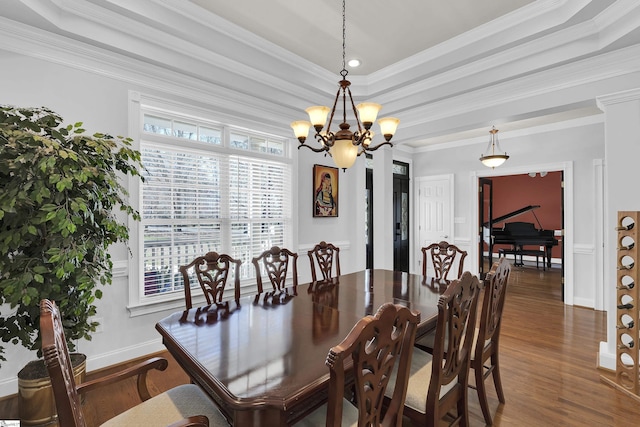 dining room with ornamental molding, dark wood-type flooring, a chandelier, and a raised ceiling