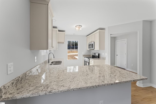 kitchen with light wood-type flooring, kitchen peninsula, sink, light stone counters, and appliances with stainless steel finishes