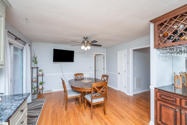 dining space with light hardwood / wood-style flooring, ceiling fan, and a textured ceiling