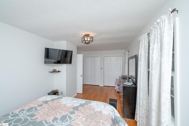 bedroom featuring light hardwood / wood-style flooring, a textured ceiling, and two closets