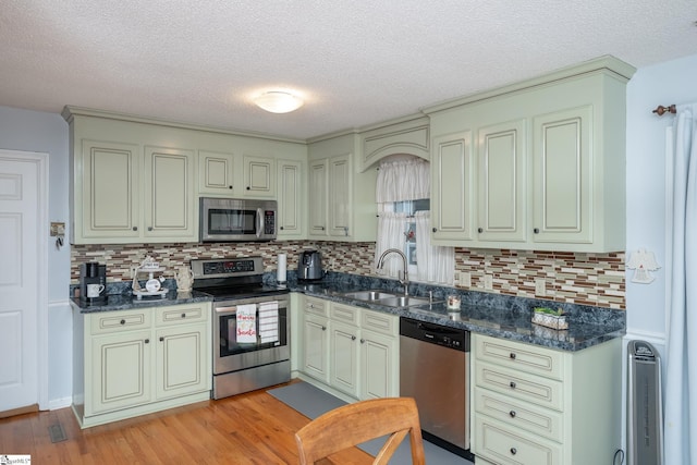 kitchen featuring tasteful backsplash, stainless steel appliances, light hardwood / wood-style floors, sink, and dark stone countertops