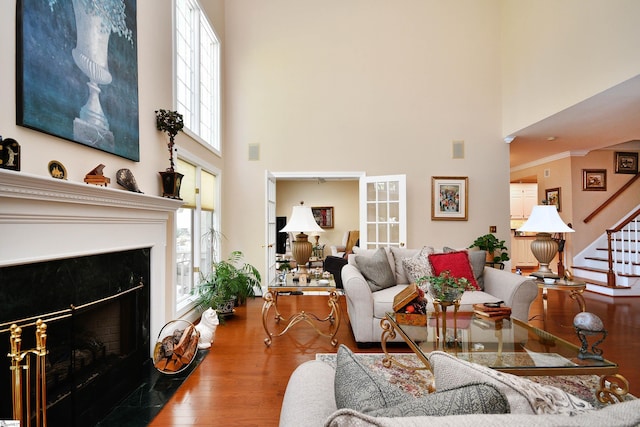 living room with a high ceiling, crown molding, wood-type flooring, and a premium fireplace